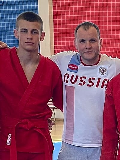 Павел Мазин в красной куртке самбо рядом с тренером Павлом Копейкиным